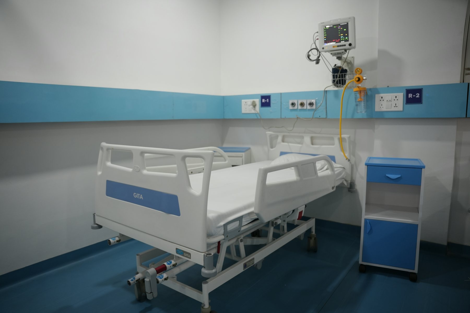 An empty ward bay with adjustable beds and a blue wall band